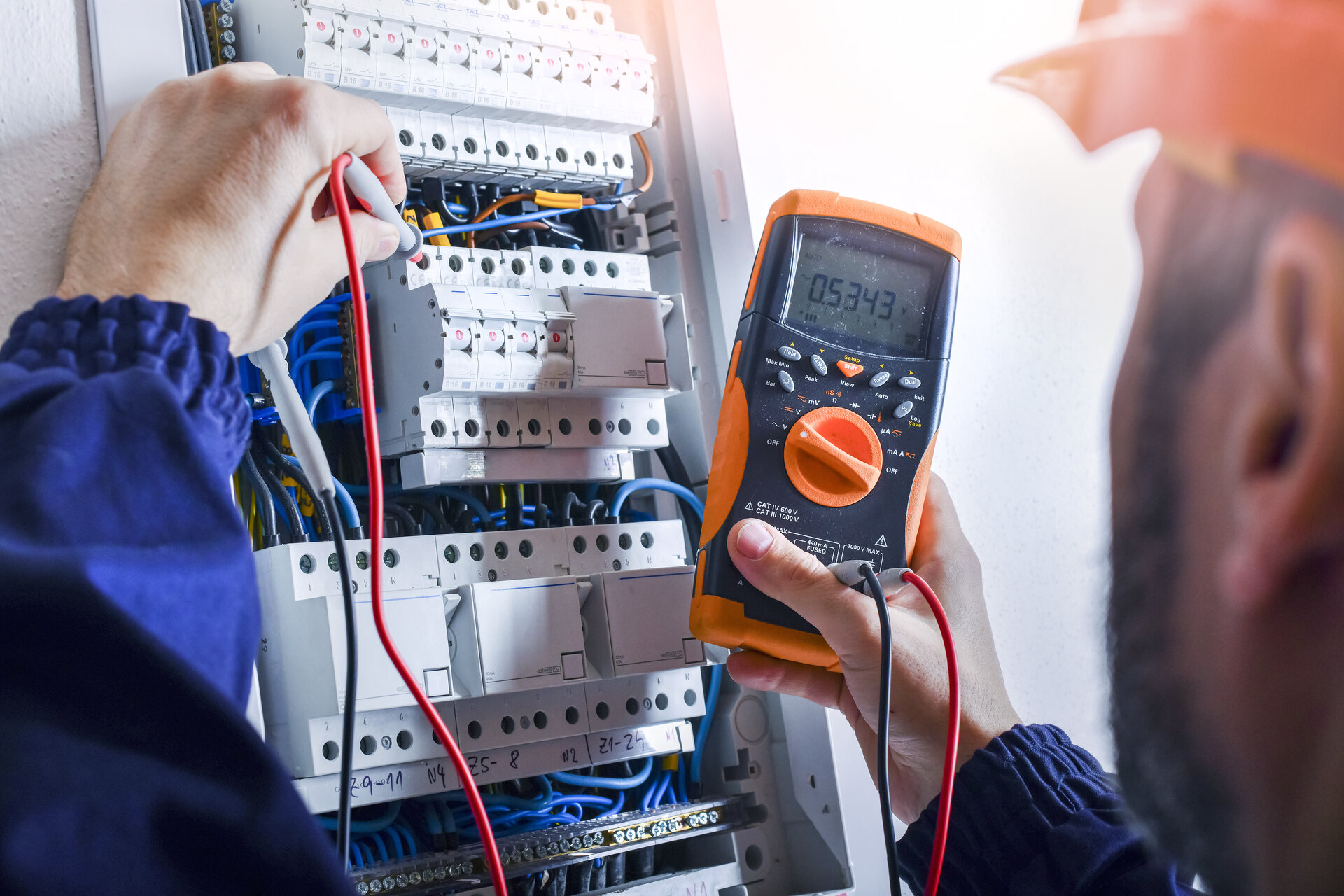 Electrician installing electric cable wires of fuse switch box. Multimeter in hands of electricians detail.